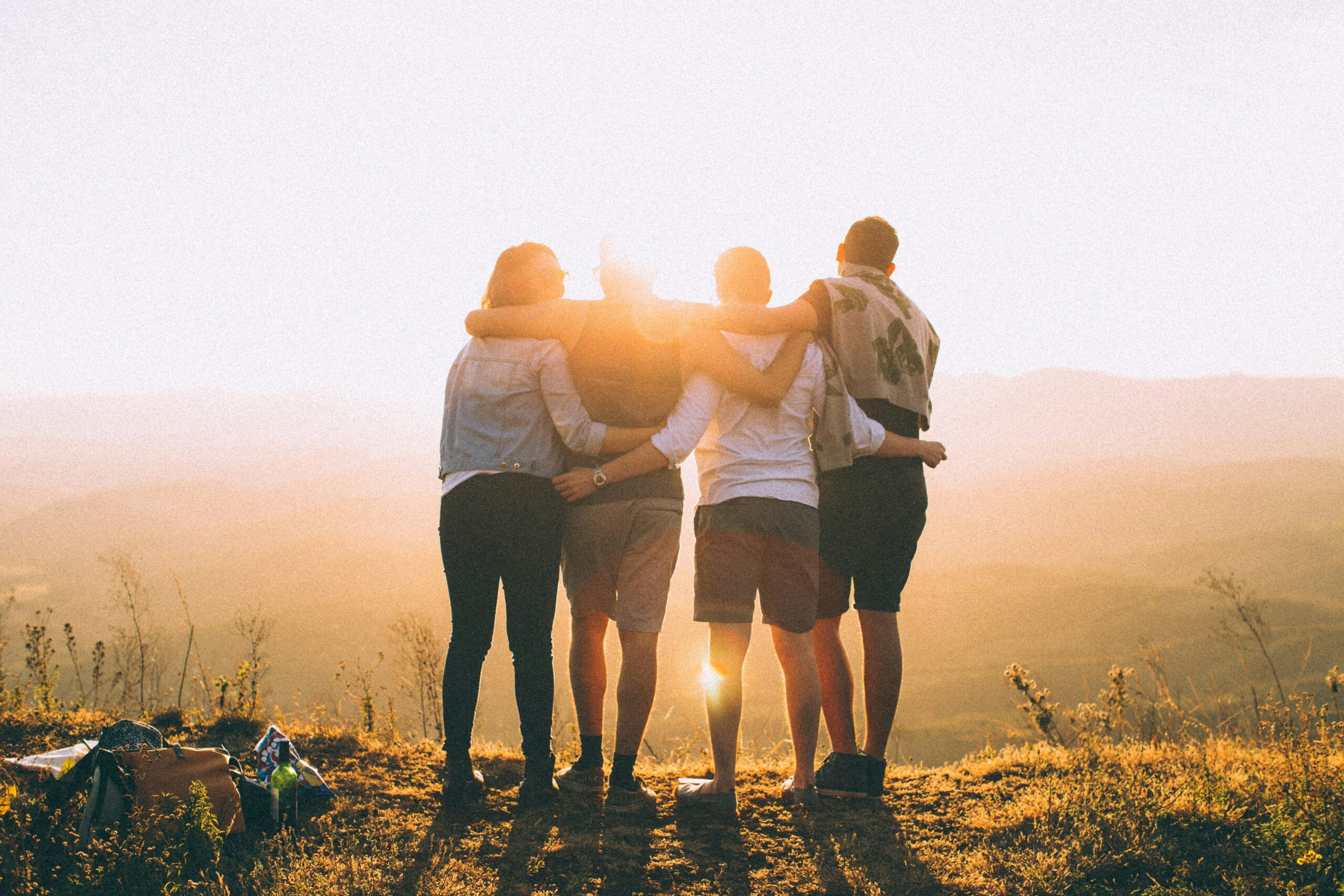 Group of people on top of a hill, facing away from the camera look towards the sunrise